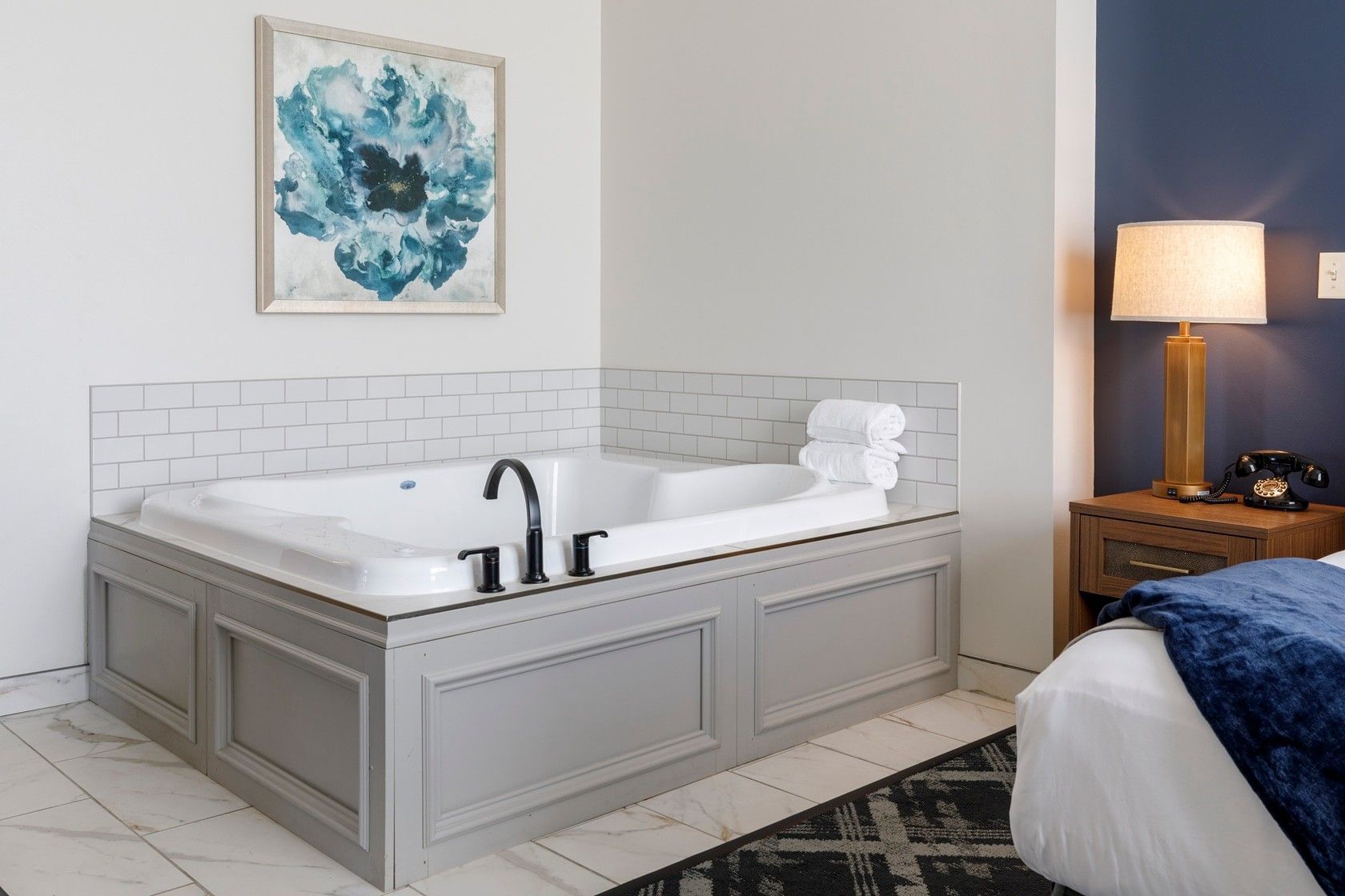 A large jacuzzi tub with a single faucet and towels on the side, next to a bed with a blue blanket