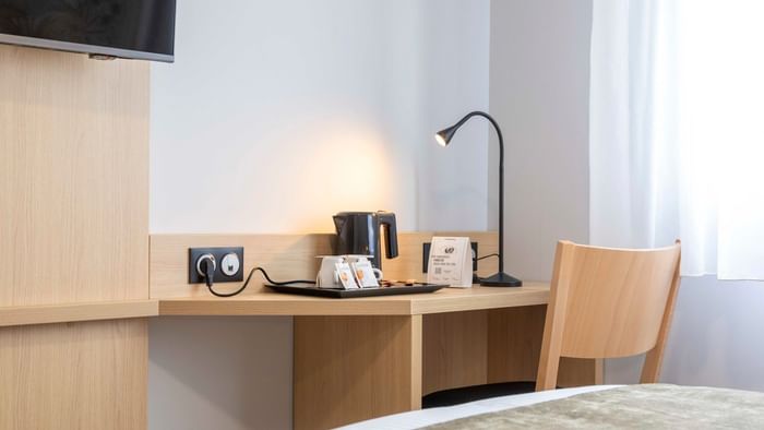 Wooden desk with lamp and coffee maker next to bed at The Originals City Hotel du Parc Gravelines