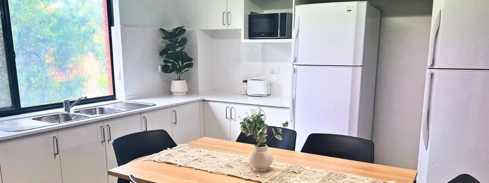 Modern kitchen with dining table and white appliances at UniLodge at Curtin University Erica Underwood House in Karawara.