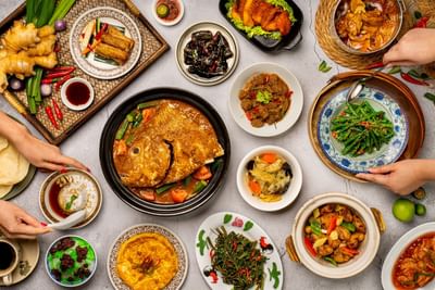 Top view of Asian dishes on a table with hands serving food in White Rose Café at York Hotel Singapore