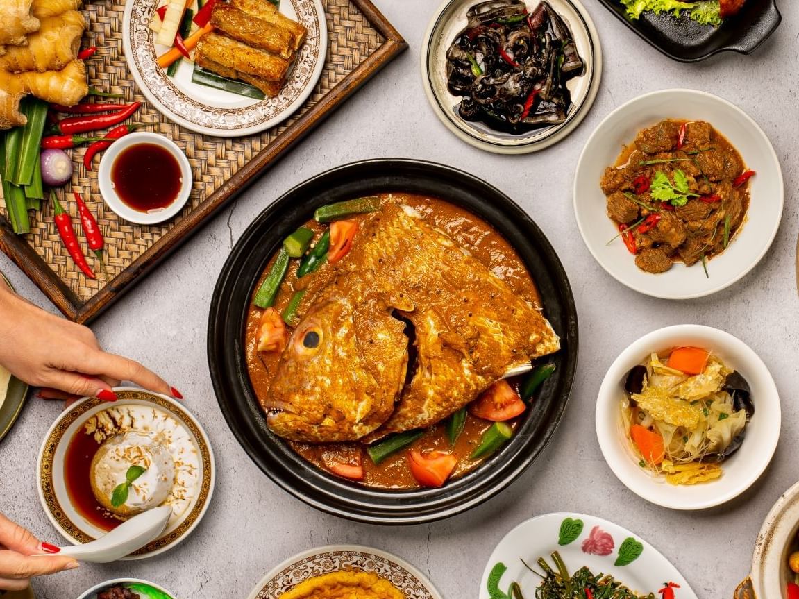 Top view of Asian dishes on a table with hands serving food in White Rose Café at York Hotel Singapore