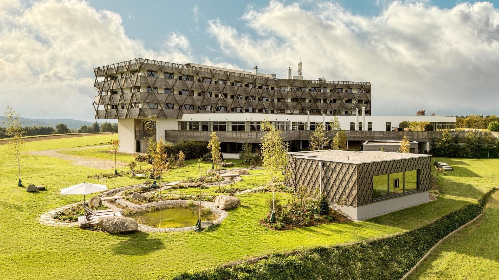 Modernes Hotelgebäude mit geometrischer Holzfassade umgeben von grünen Rasenflächen im Falkensteiner Hotel Bad Leonfelden