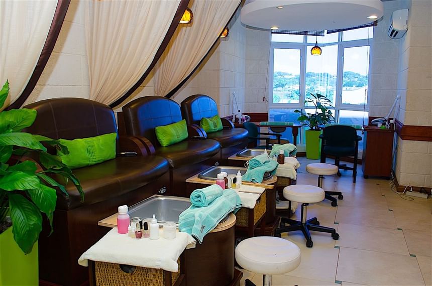 Brown pedicure chairs with green pillows by white stools in the Chakra Spa at Accra Beach Hotel & Spa