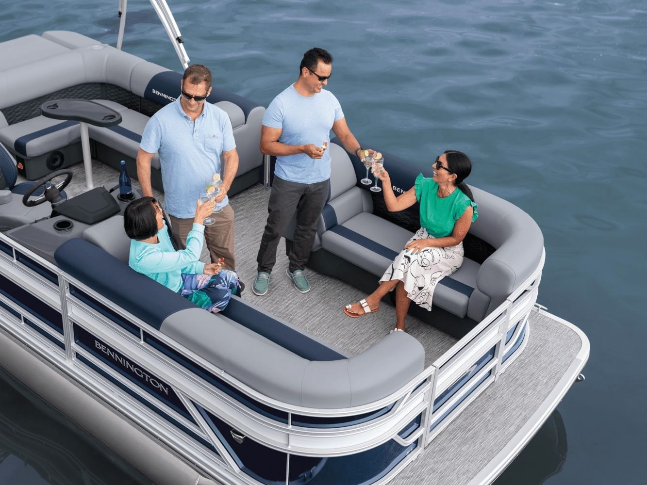 Four people enjoying drinks and conversation on a modern pontoon boat with gray seating on calm blue water
