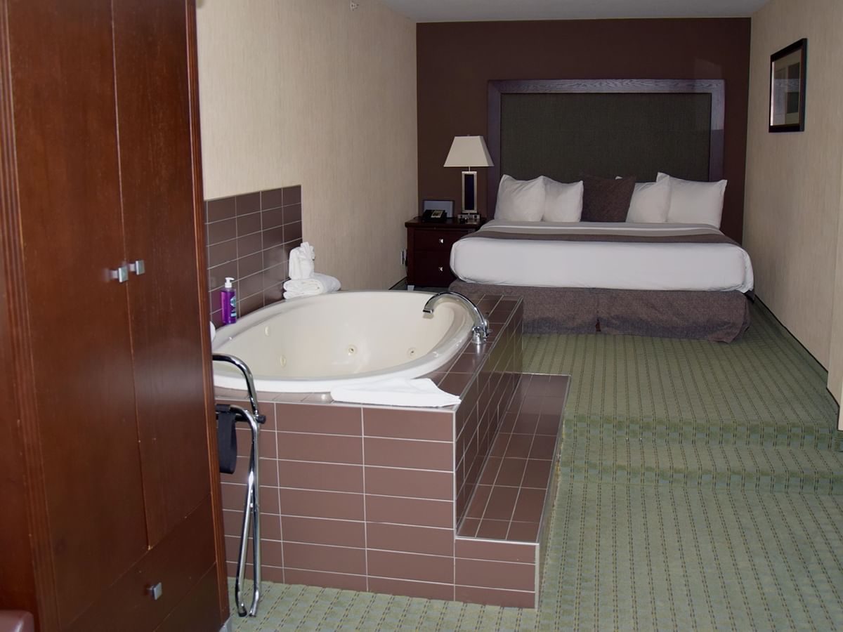 Hotel room with a large bed, a tub, and a wooden closet.