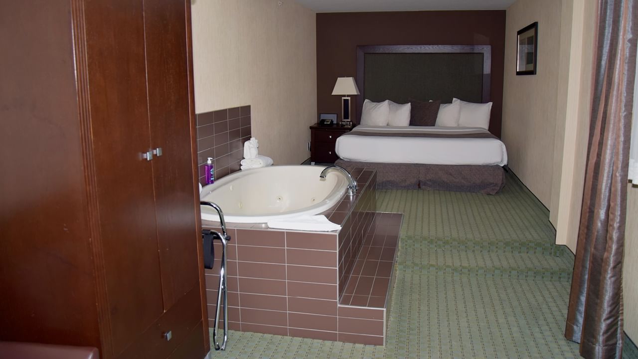 Hotel room with a large bed, a tub, and a wooden closet.