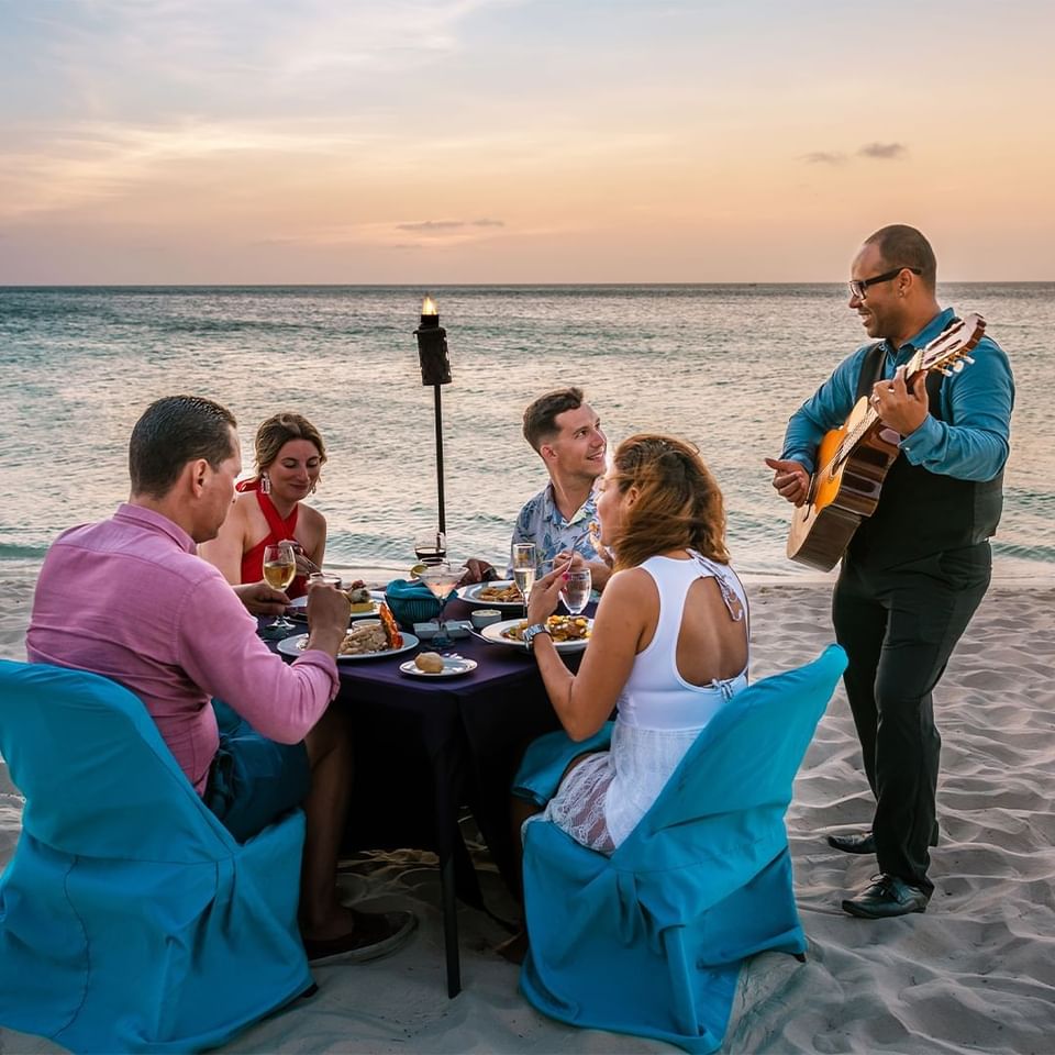 Group of people dining at Couple sitting under the fofoti tree at Passions on the Beach - Eagle Beach with guitar player