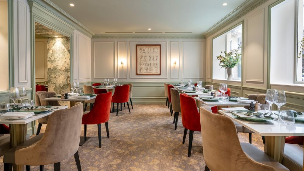 Dining room featuring tables surrounded by red and beige velvet chairs in Le Céladon at Hotel Westminster Paris