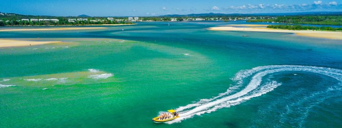 Speedboat with passengers glides through turquoise waters framed by lush greenery near the Novotel Sunshine Coast Resort