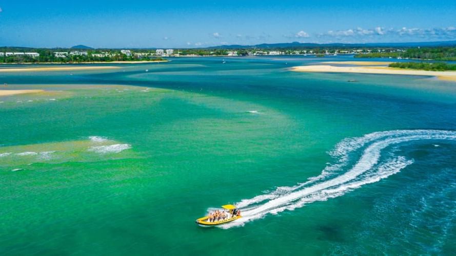 Speedboat with passengers glides through turquoise waters framed by lush greenery near the Novotel Sunshine Coast Resort