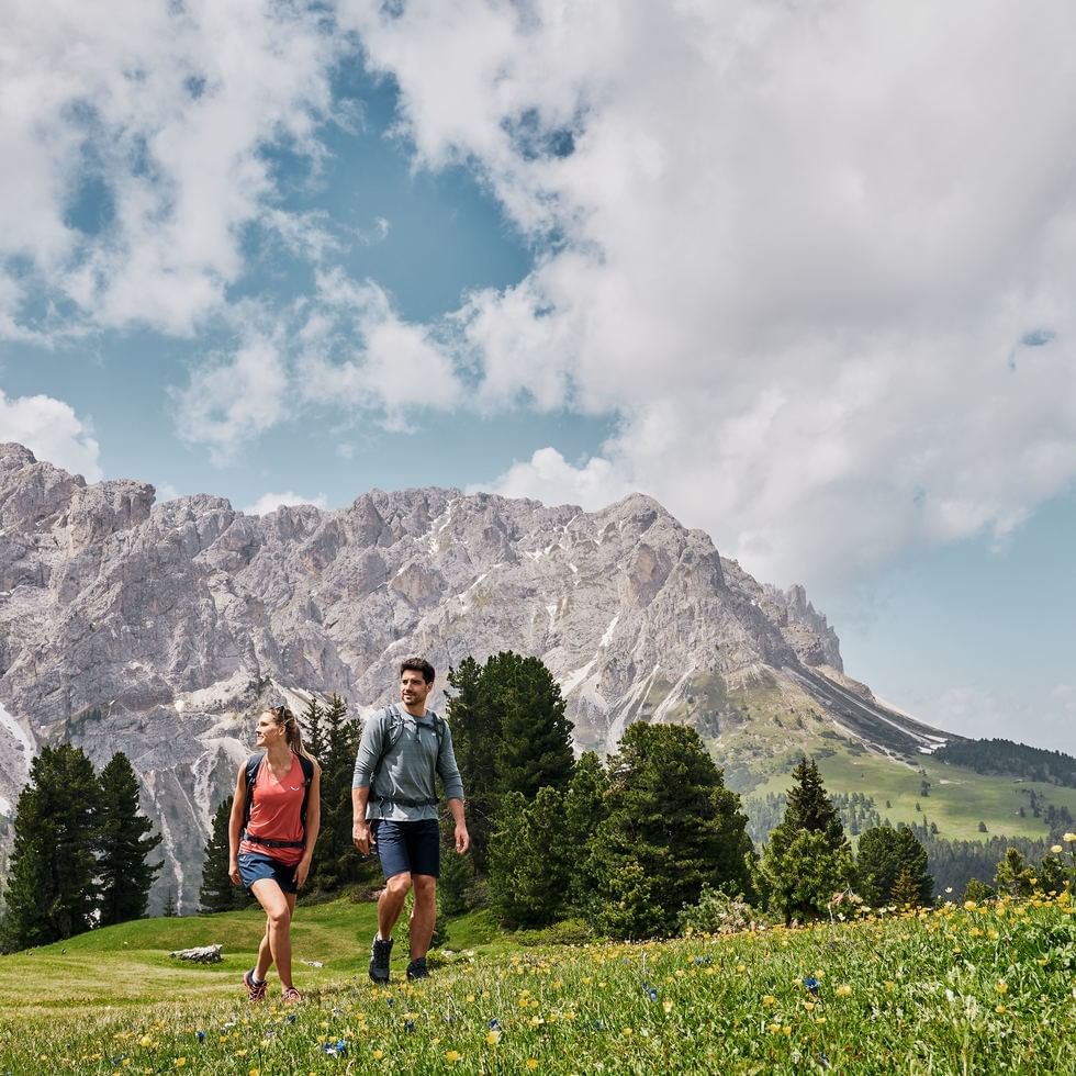 Couple hiking through wildflowers in front of majestic mountains promoting Spring Getaway in Terenten.