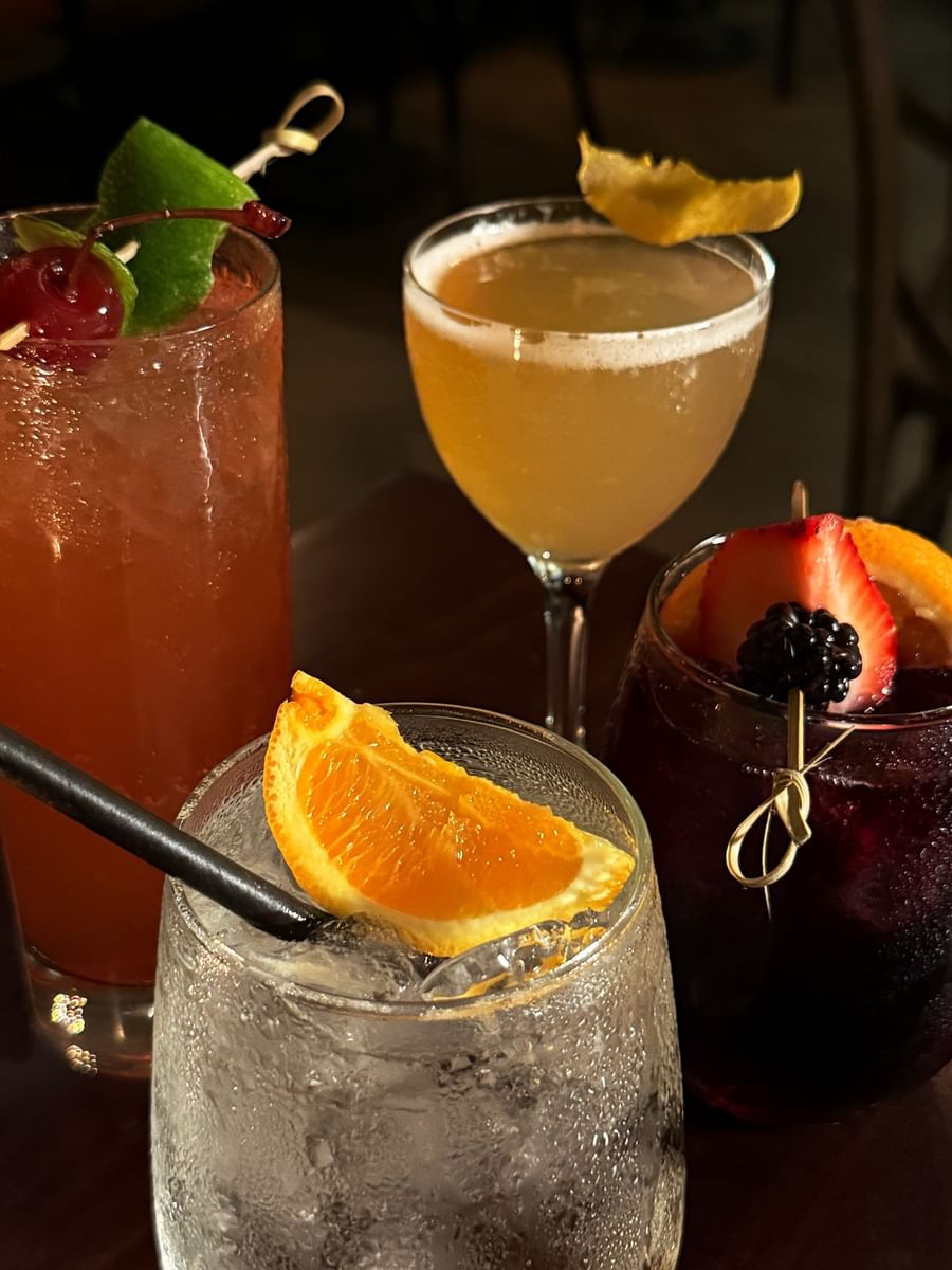 Colorful cocktails with fruit garnishes by a glass of citrus juice in The European at Warwick San Francisco
