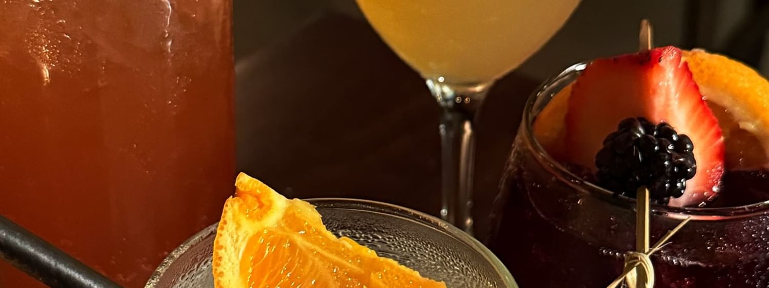 Colorful cocktails with fruit garnishes by a glass of citrus juice in The European at Warwick San Francisco