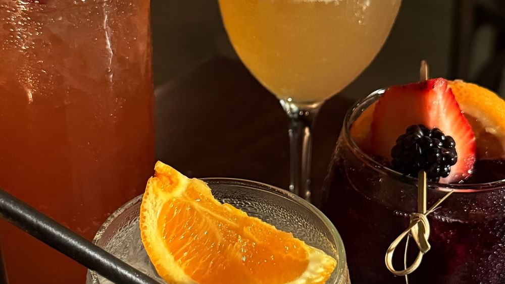 Colorful cocktails with fruit garnishes by a glass of citrus juice in The European at Warwick San Francisco