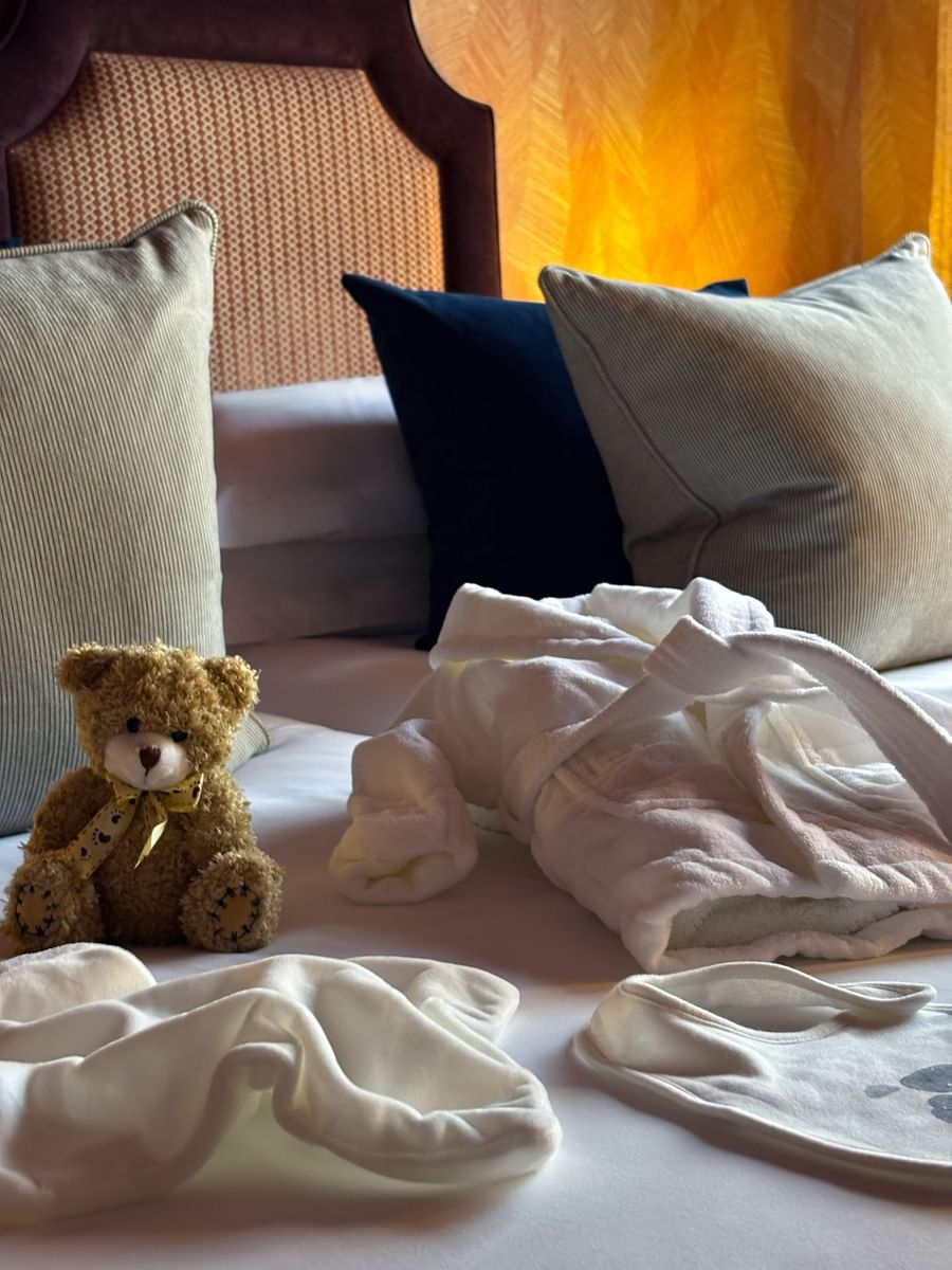 Teddy bear placed on a bed, by a plush white robe at The Capital Hotel, Apartments and Townhouse