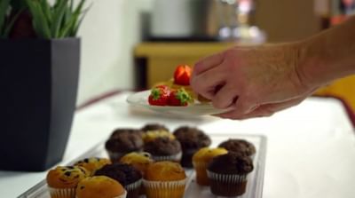A hand adds strawberries to a plate next to a muffin tray with a potted plant on the breakfast table at Moab Valley Inn
