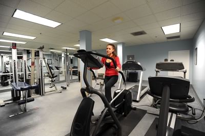Woman exercising on ellipticals inside a fitness center with a treadmill and weight equipment nearby at The Simsbury Inn