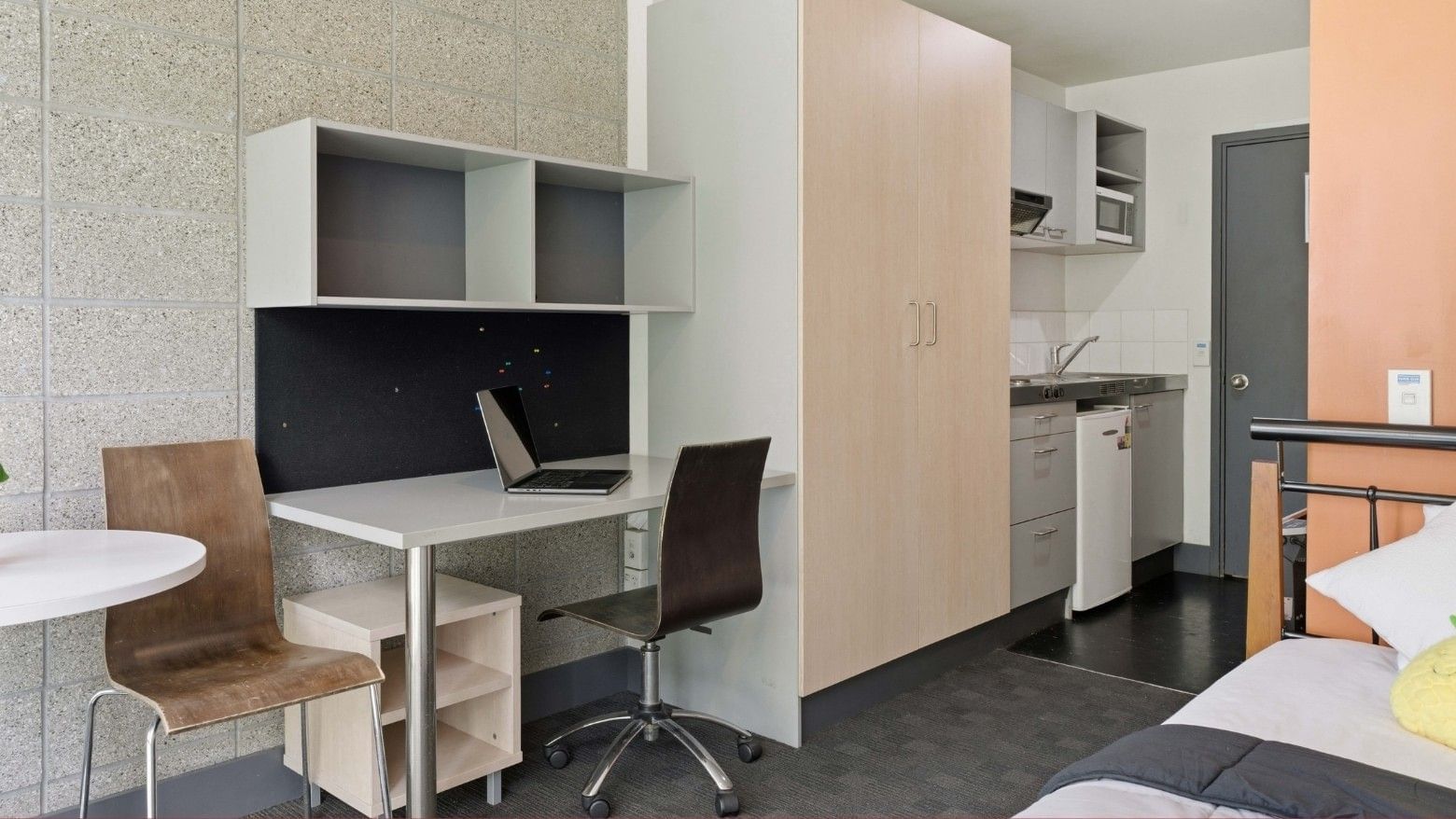 Compact student living space with desk, chair, bed, and kitchenette at Student Living Auckland - Beach.