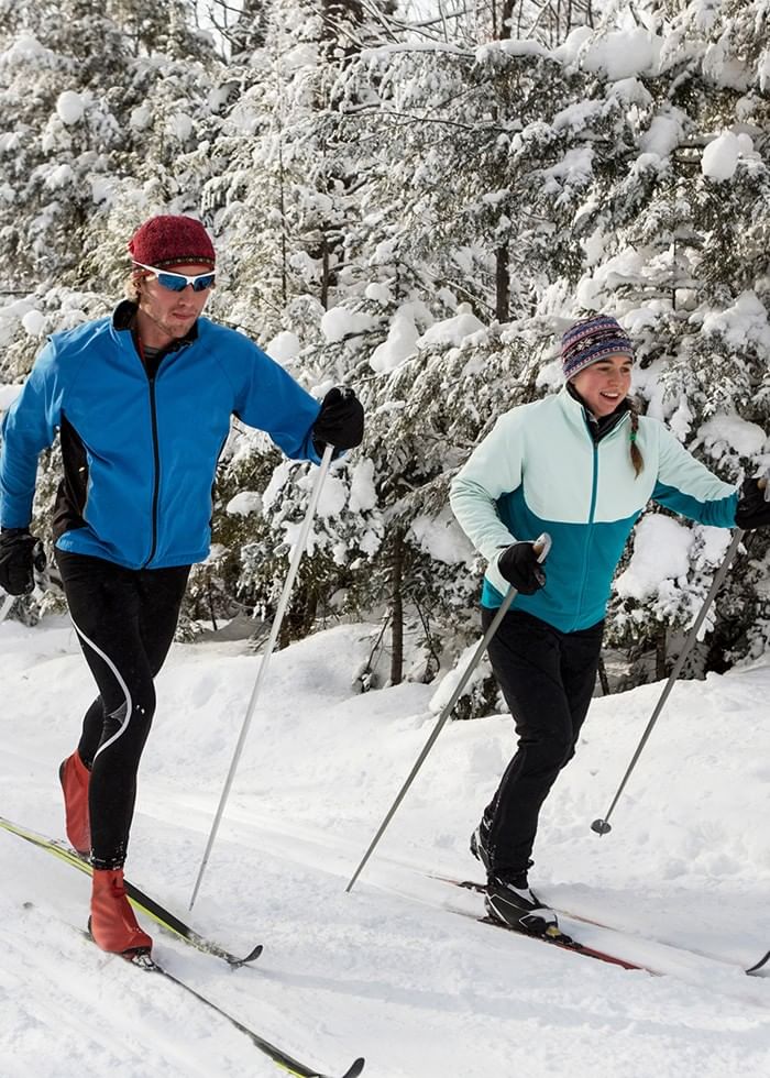 Couple skiing together through a snow-covered evergreen forest during fun things to do in London Ontario near Spencer Hotel