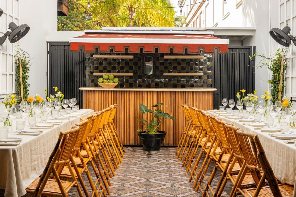 A beautifully set outdoor dining area with a bar, tables, chairs, flowers, and wine glasses.