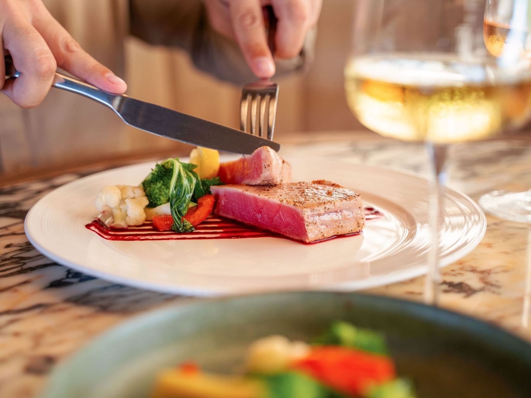 Close-up of a person slicing a tuna steak, garnished with vegetables and a drizzle of sauce, served at Golden Rock Resort