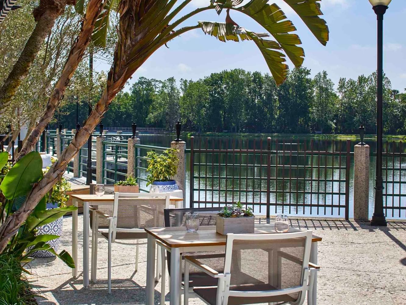 Waterfront patio of The Inn at Celebration with wooden tables & white chairs under palm fronds, hotels in Celebration FL