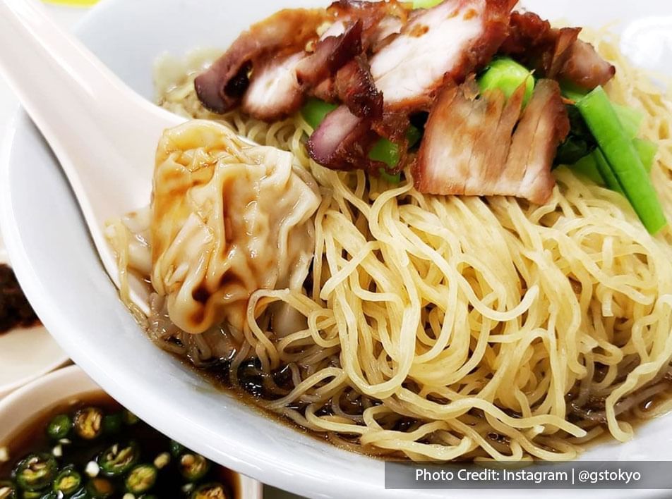wantan mee is a dish of egg noodles in a black sauce, topped with dumplings, slices of char siu, and boiled choi sum