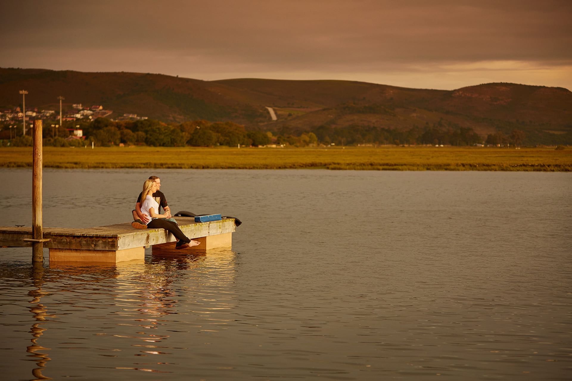 A couple sitting at the pier by the lake near Knysna River Club