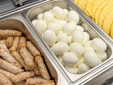 Trays of breakfast foods including eggs, sausages, and pastries in a buffet setup.