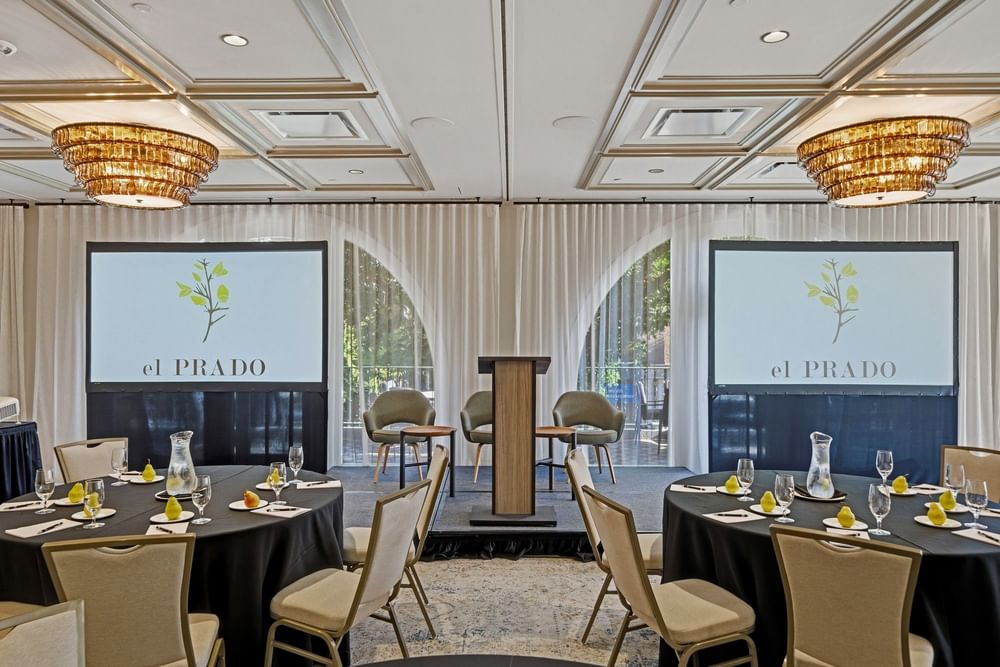 meeting room set up at el PRADO with projected screens towards the front of the room, alongside a speaker podium