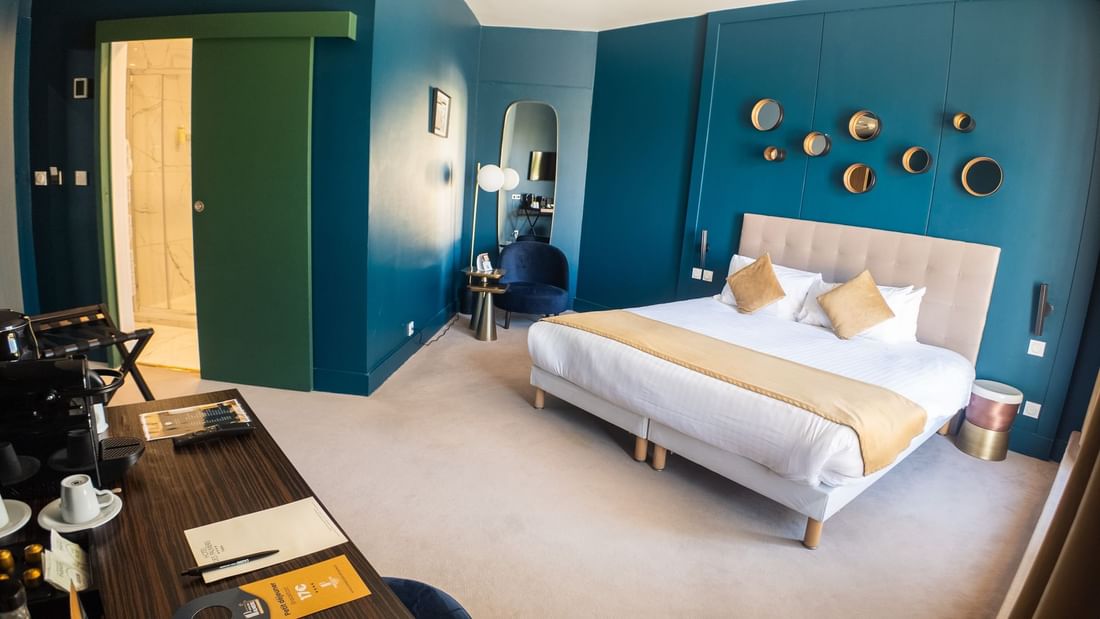 Chambre élégante avec lit double, bureau, chaise bleue et murs bleus décorés de cercles dorés.