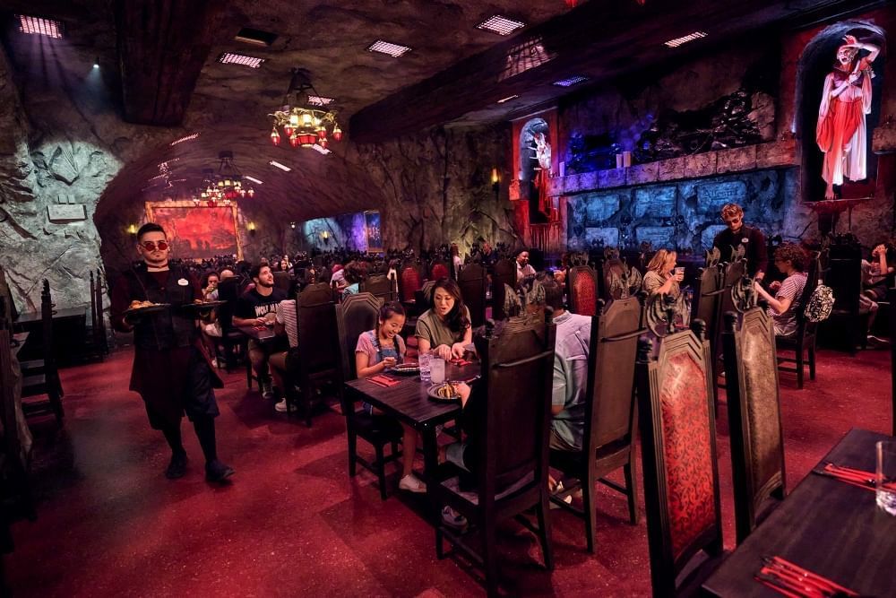 A creepy, cave-like restaurant with red carpet, bloody statues against the wall, and waiters wearing dark clothing and makeup.