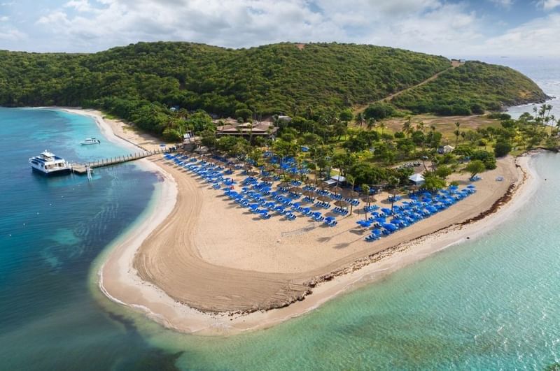 High-angle view of Palomino Island featuring blue umbrellas along sandy beaches managed by El Conquistador Resort