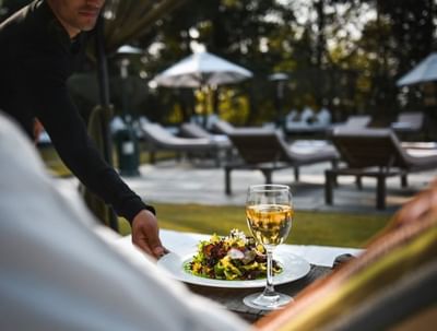 Waiter serves a fresh salad & a glass of wine outdoors in Ananta Poolside Restaurant at The Dwarika's Himalayan Wellbeing