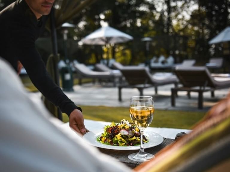 Server serving a salad and a glass of white wine to a guest in Ananta Poolside Restaurant at Dwarika's Himalayan Wellbeing
