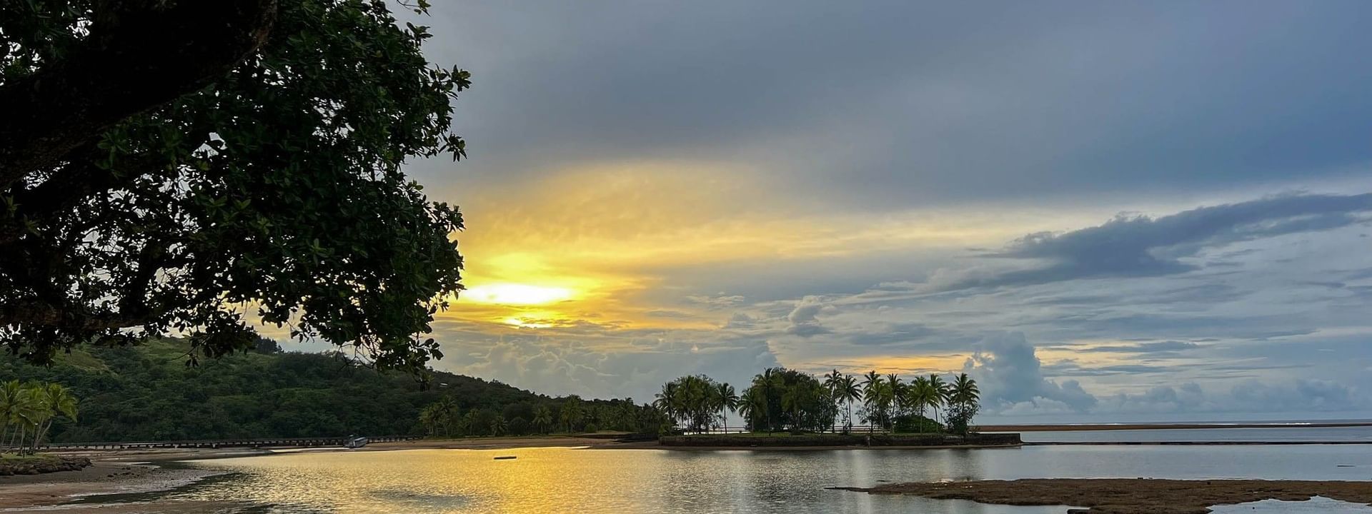 Golden sunset by a calm bay with palm trees on an island under cloudy skies near The Naviti Resort in Korolevu, Fiji