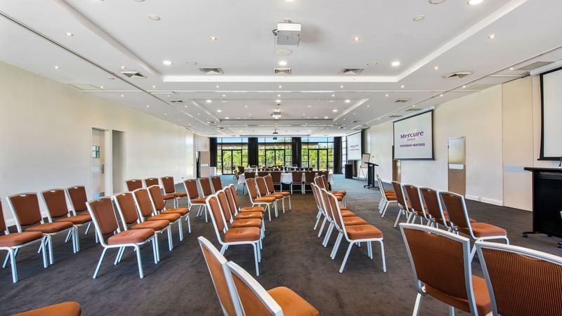 Kooindah Ballroom with rows of orange chairs and a presentation screen at Mercure Kooindah Waters