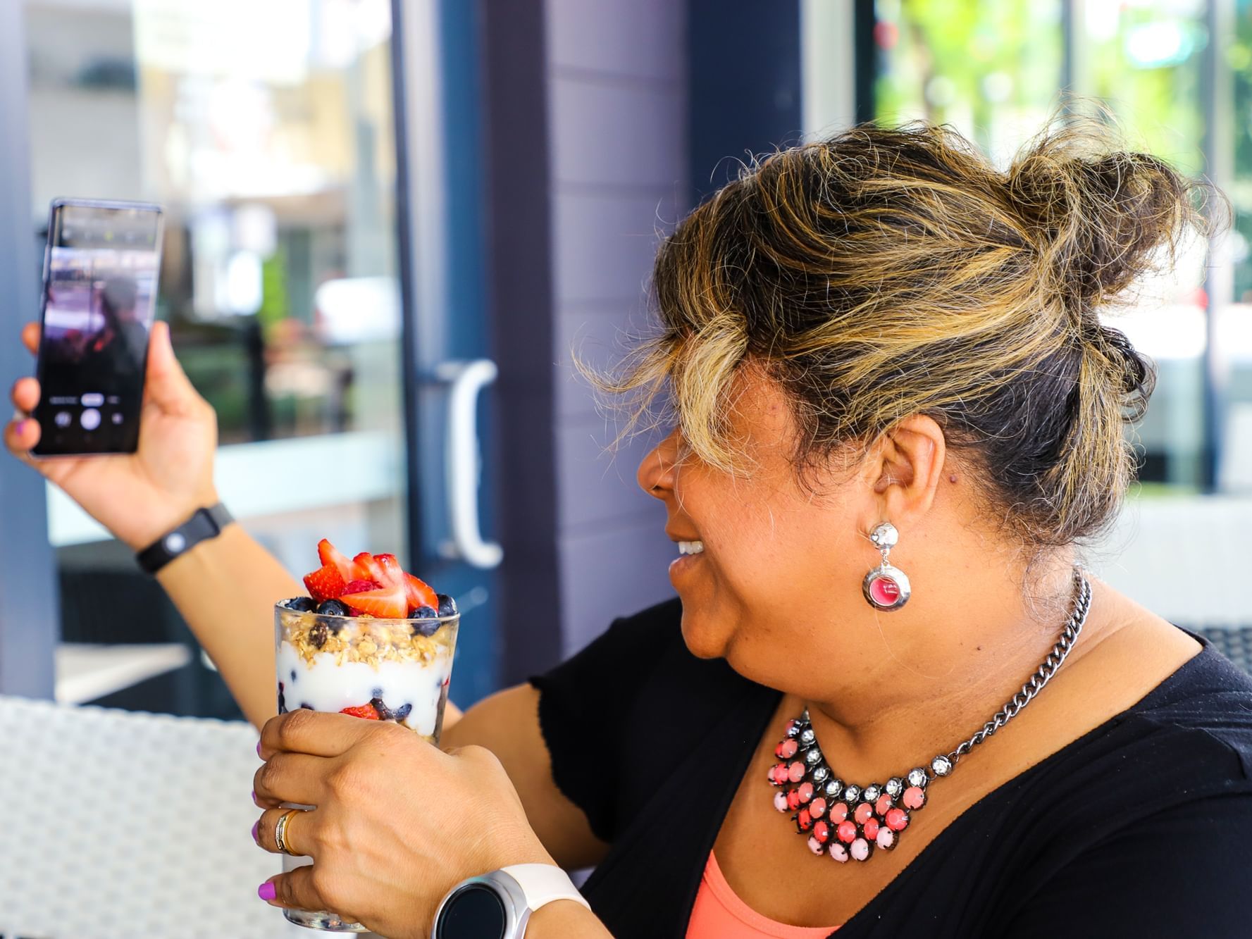 A woman holds a colorful dessert topped with berries and granola, while taking a selfie in Riverside Hotel Fort Lauderdale