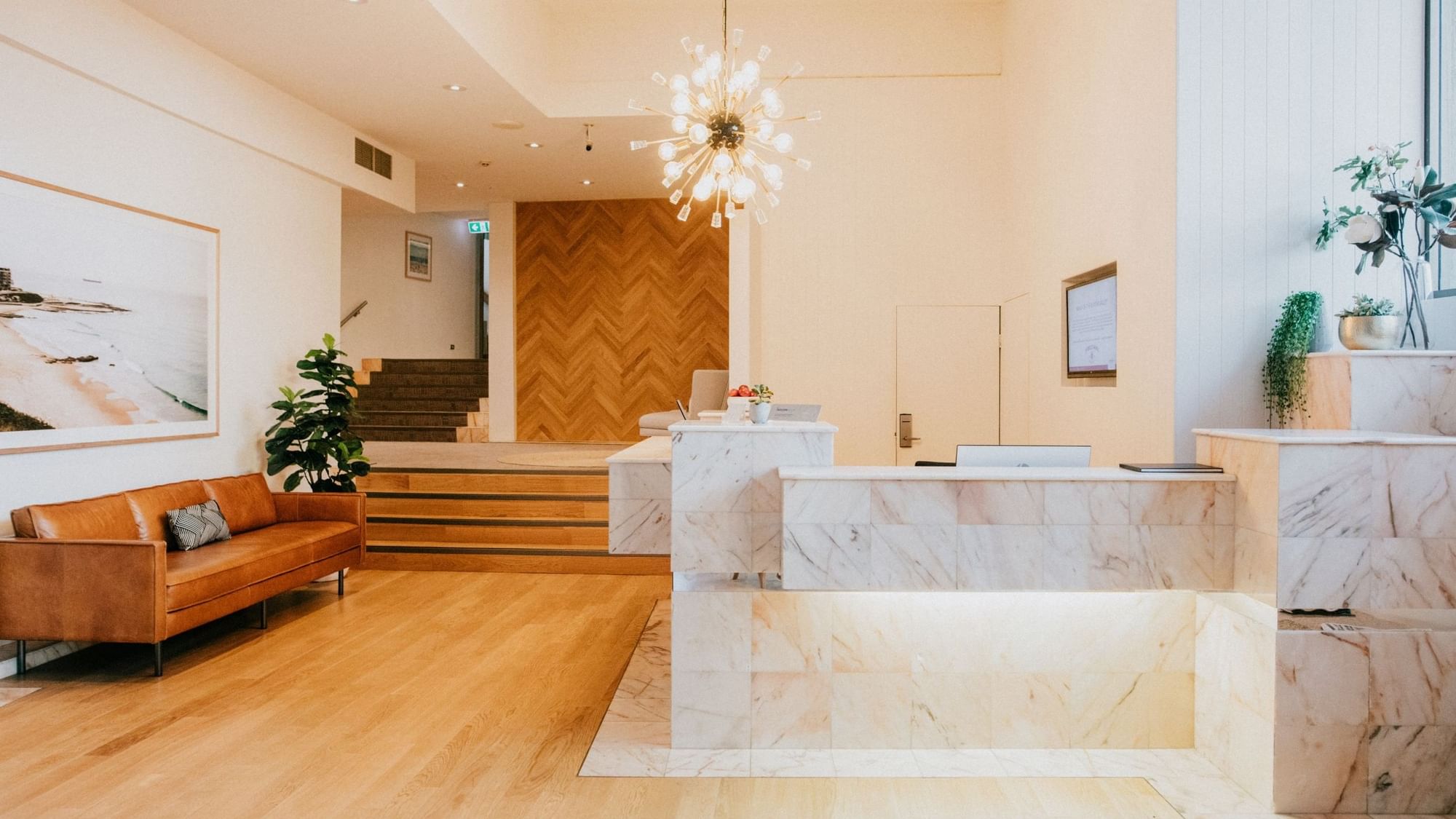 Elegant lobby with a marble reception desk, modern chandelier, and brown couch at Mercure Charlestown.