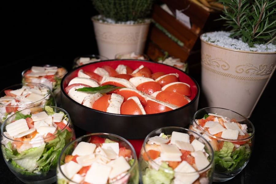 Un saladier de salade caprese et des portions individuelles de salade présentées dans des coupelles, entourées de plantes en pot, au Warwick Paris Champs-Élysées