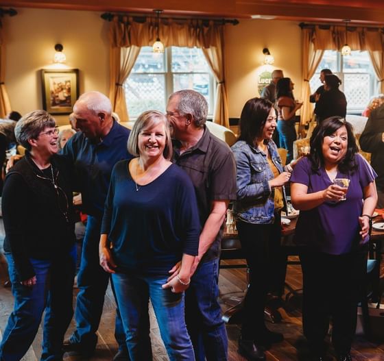 Group of happy guests gathering by dining tables under warm pendant lamps at Oregon Garden Resort