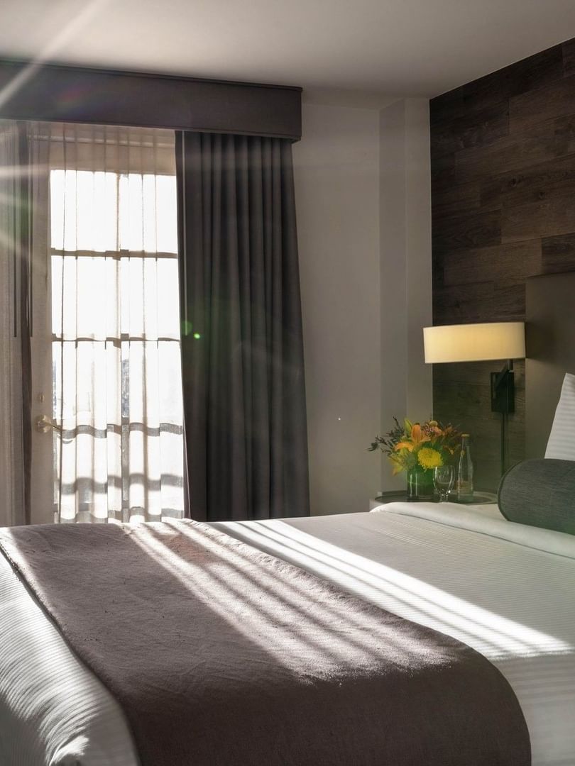 King bed by a side table under a wood-paneled wall in a sunlit room in Executive Suites at Warwick Denver