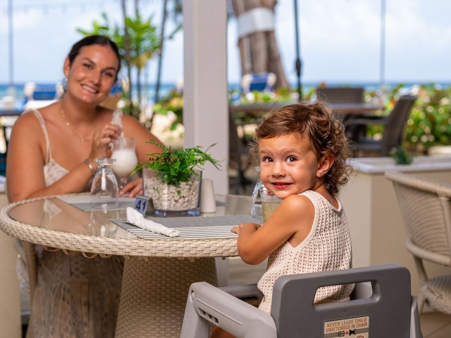 Woman and child sitting at table with ocean view at Savannah Beach Hotel.