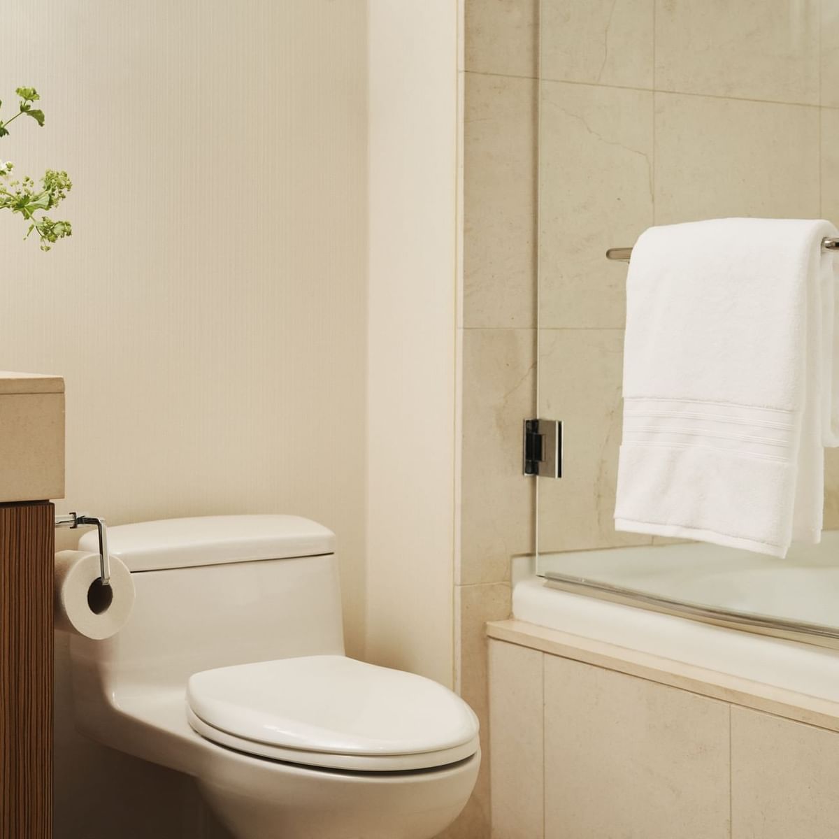Toilet and bathtub in a bathroom with a vase of flowers on the counter and a towel hanging by the shower.