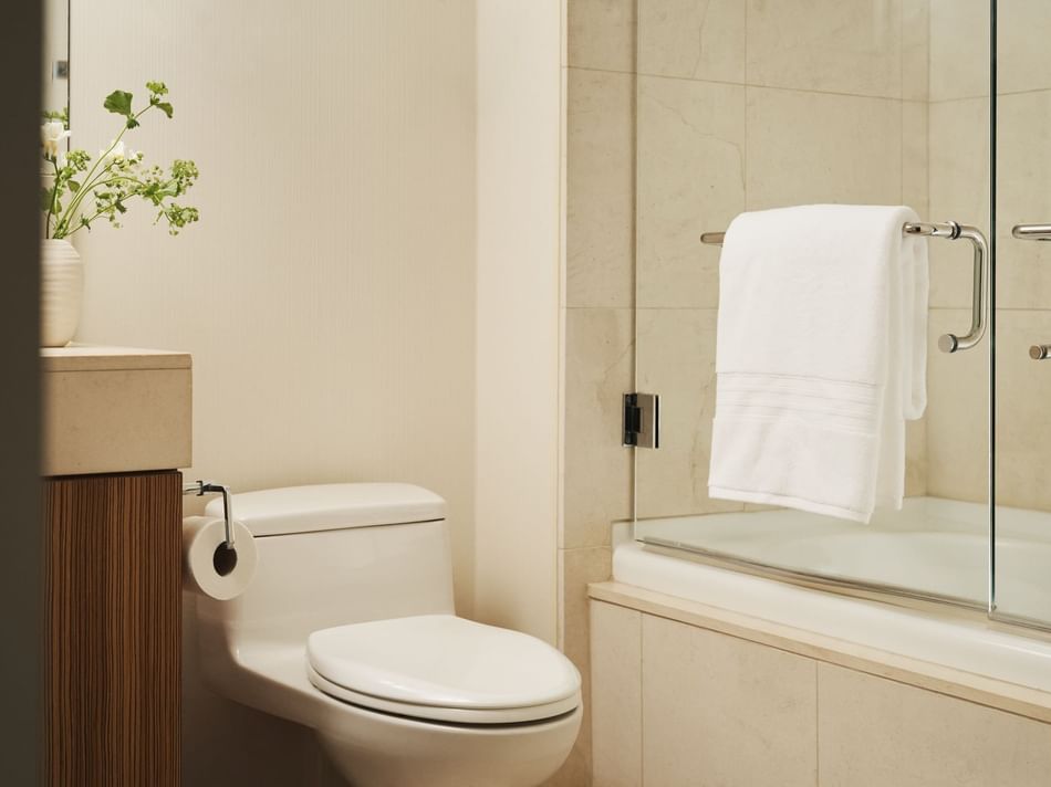 White toilet, wooden cabinet, towel rack, and glass shower enclosure in a bathroom with a vase of flowers.