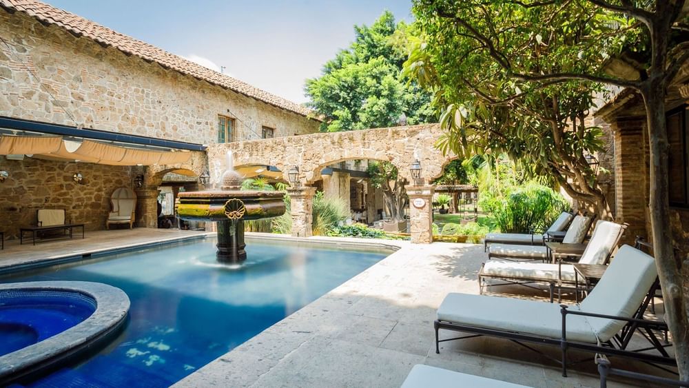 Outdoor pool area with a stone fountain and white lounge chairs at Quinta Real Guadalajara
