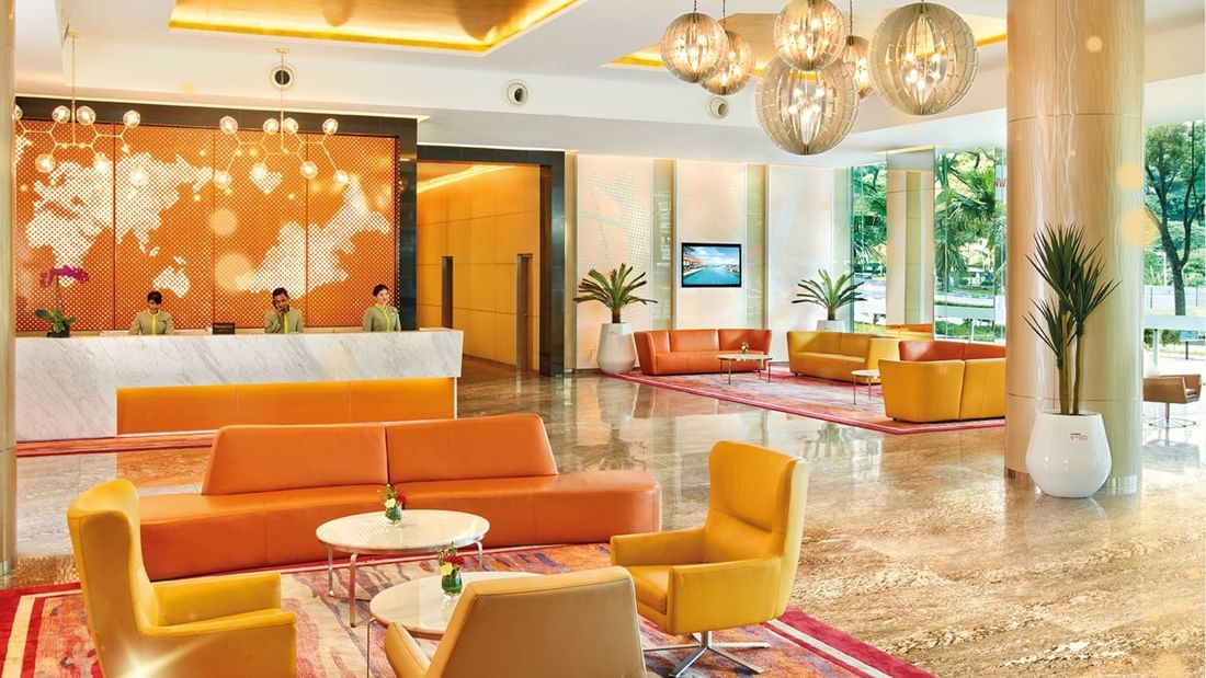 Modern hotel lobby with orange couches, yellow chairs, and a reception desk with three staff members.