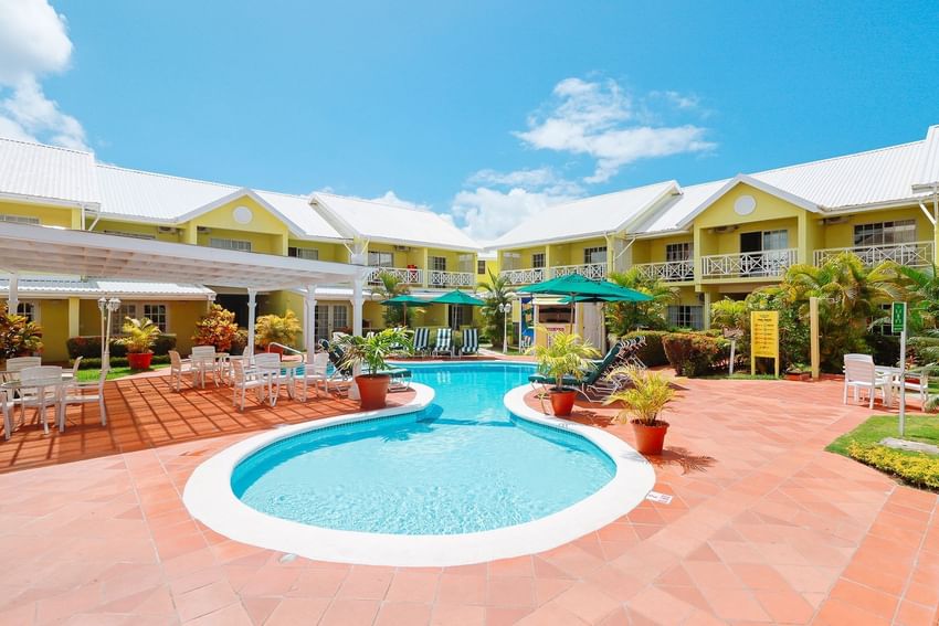 Scenic curved pool area at Bay Gardens Hotels and Resorts with lounge chairs, and buildings on a sunny day under blue sky