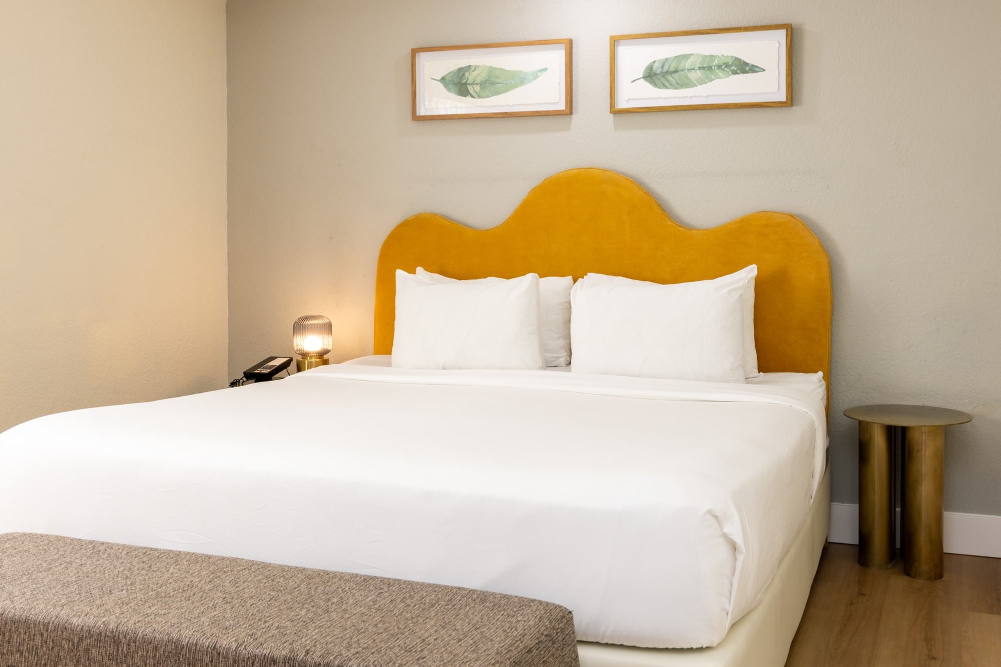 A hotel room with a large bed, yellow headboard, and two framed pictures on the wall.
