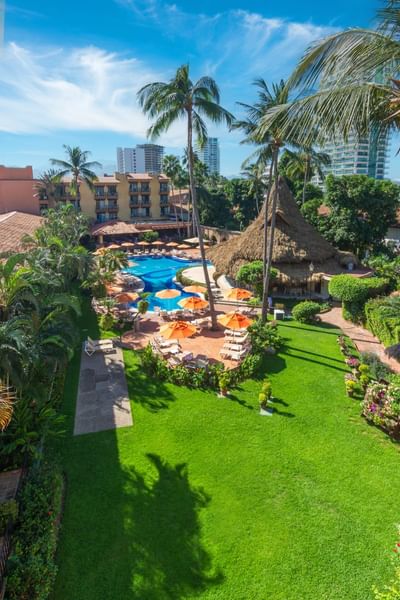 Aerial view of a resort with pool, lounge chairs, palm trees, and thatched roof hut.